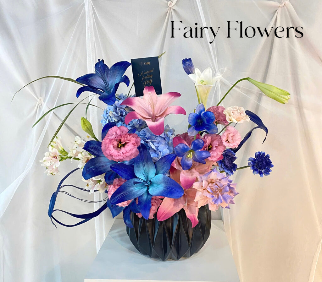 🌌 Bình Hoa Nghệ Thuật Tông Xanh Tím Hồng – Dấu Ấn Của Sáng Tạo Và Cá Tính Tựa như một bức tranh ấn tượng mang sắc màu hoàng hôn rực rỡ, bình hoa phối màu độc đáo từ Fairy Flowers là sự kết hợp đầy nghệ thuật giữa hoa ly xanh – ly hồng – hồng tím – cẩm tú cầu – hoa thủy tiên và các loại hoa phụ thanh thoát. Từng cánh hoa mang một sắc độ riêng biệt nhưng không hề rời rạc – tất cả cùng nhau tạo nên một tổng thể tràn đầy cảm hứng và cá tính. 💐 Thiết Kế Mạnh Mẽ – Cá Tính Nhưng Vẫn Mềm Mại Hoa được cắm khéo léo theo kiểu asymmetrical balance (bố cục bất đối xứng hiện đại), tạo chuyển động cho ánh nhìn và chiều sâu cho tác phẩm. Sắc xanh cobalt, tím violet, hồng ngọt ngào cùng chiếc bình đen hiện đại làm nổi bật chất "high-fashion" trong thiết kế, phù hợp với những ai yêu cái đẹp độc đáo, khác biệt.